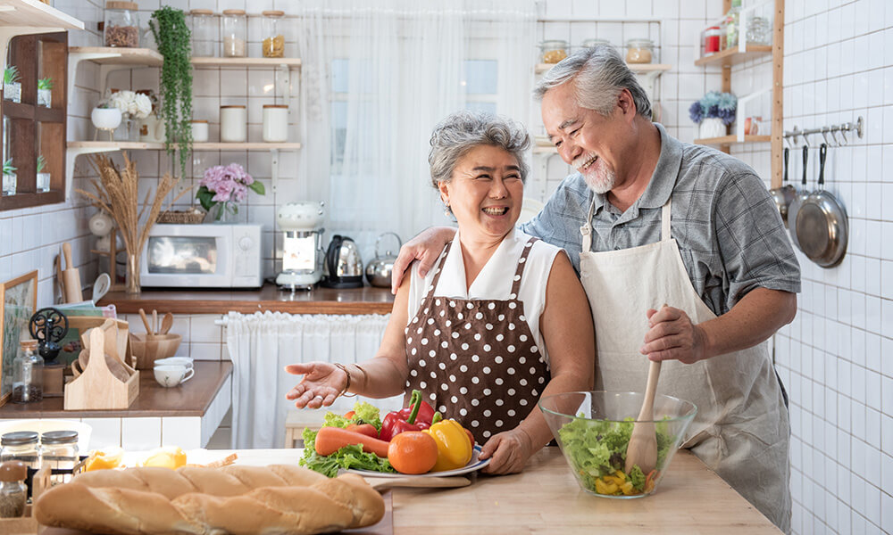 a senior couple while cooking at a kitchen
